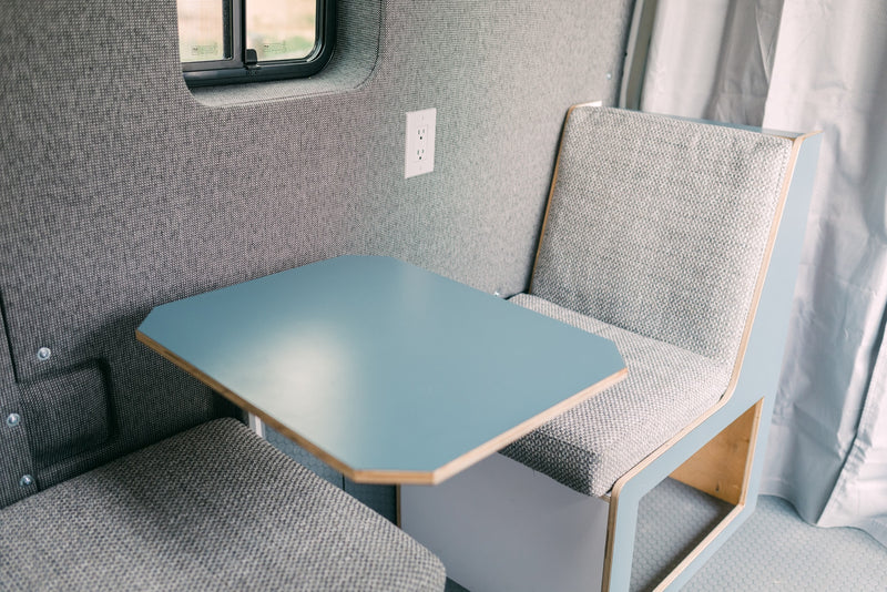 Modern RV rental interior with light gray upholstered seating, blue table, and window. A compact, efficient travel space. — photo 12