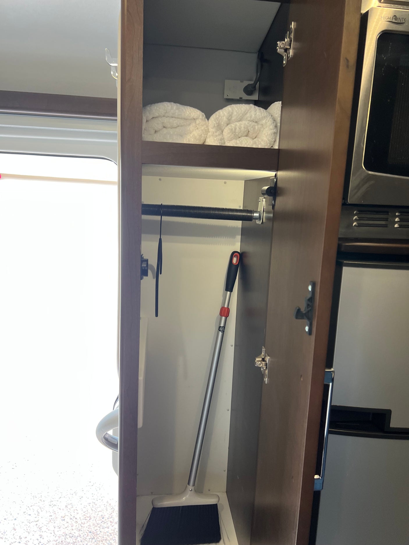 RV rental: Organized cabinet with rolled towels, broom, and kitchen appliances maximizing compact storage space.