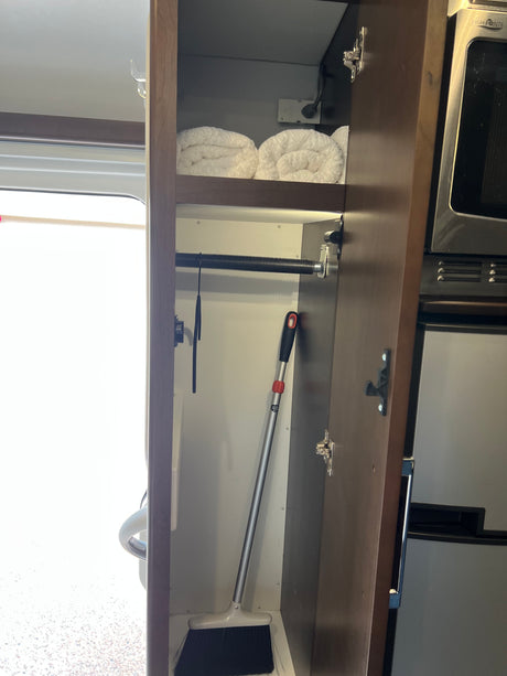 RV rental: Organized cabinet with rolled towels, broom, and kitchen appliances maximizing compact storage space.