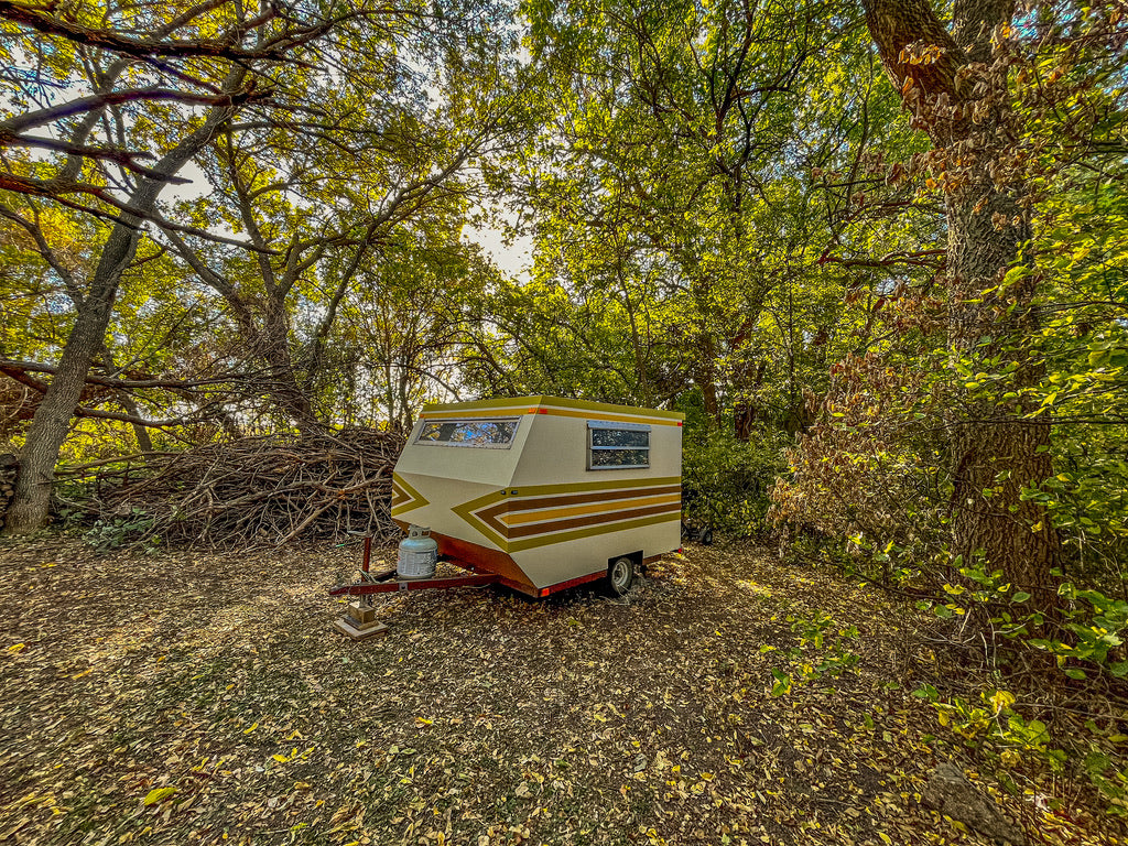 A charming vintage camper, ideal for your next RV rental adventure, parked amidst autumn leaves and sun-dappled trees.