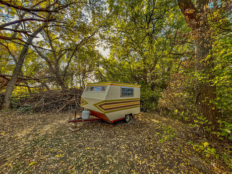 A charming vintage camper, ideal for your next RV rental adventure, parked amidst autumn leaves and sun-dappled trees.