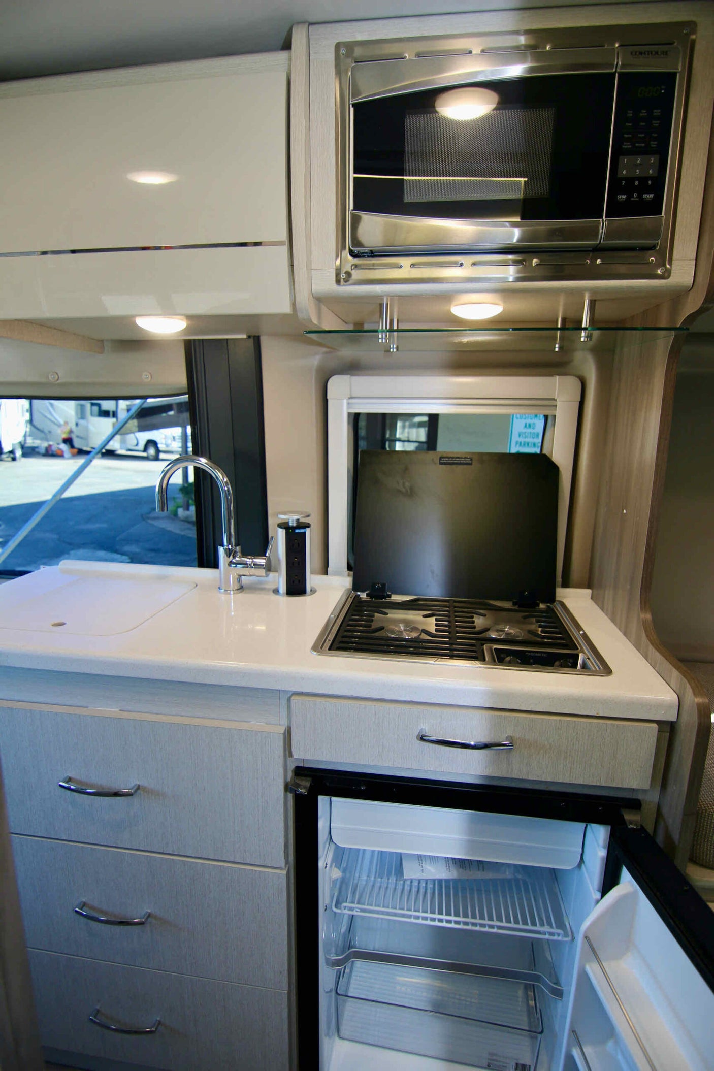This bright, modern RV rental kitchen includes a microwave, sink, stovetop, and an open refrigerator.