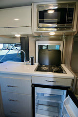 This bright, modern RV rental kitchen includes a microwave, sink, stovetop, and an open refrigerator.