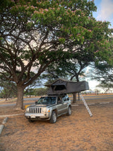Experience camping with this unique RV rental: a Jeep Patriot with a deployed rooftop tent under blooming trees.