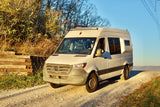 A white Sprinter van on a scenic dirt road, ready for adventure. Explore the outdoors with this RV rental!