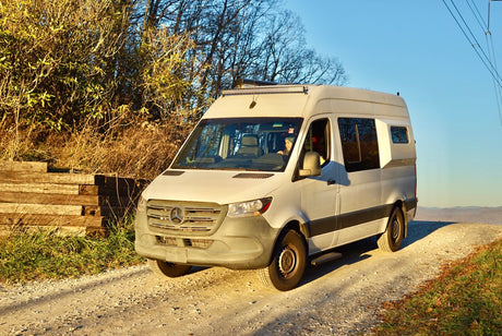 A white Sprinter van on a scenic dirt road, ready for adventure. Explore the outdoors with this RV rental!