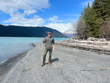 Man on a pebble beach by a turquoise lake and snowy mountains, perfect for an RV rental outdoor adventure.