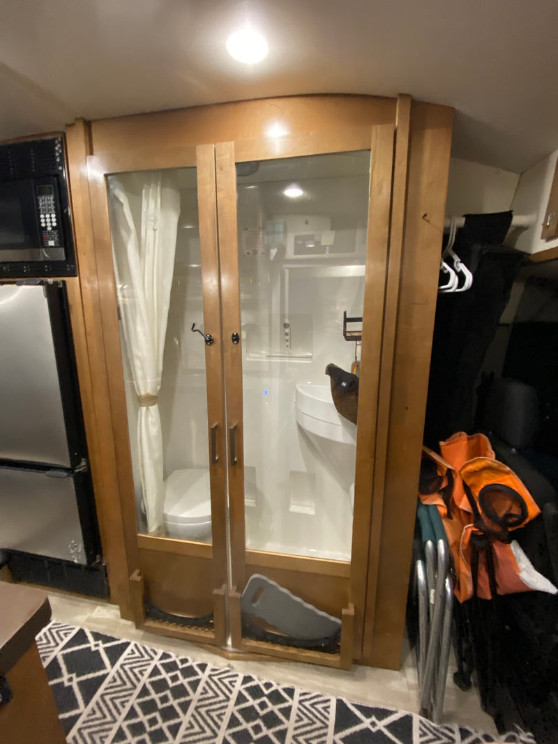 Inside an RV rental, a compact bathroom with toilet, sink, and shower is visible through glass doors, next to kitchen appliances. — photo 8