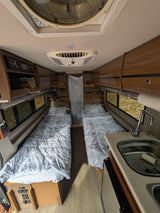 Inside this cozy rv rental: twin beds with patterned comforters, a compact kitchen with sink, wood walls, and overhead storage.