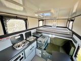 Modern rv rental interior showing a compact kitchen, comfortable bed, and versatile seating area in a pop-up camper.