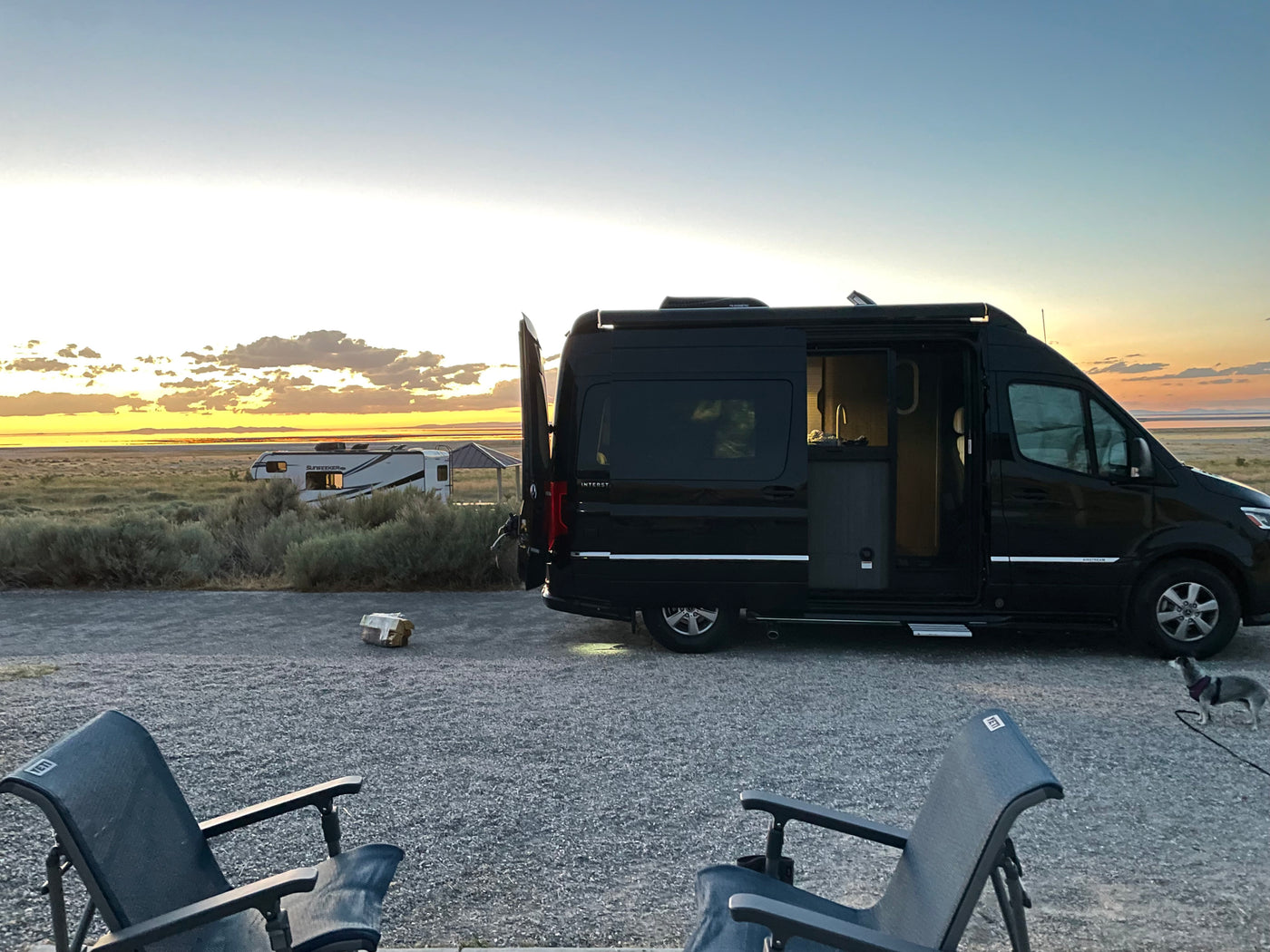 Enjoying golden hour with our Airstream RV rental camper van, outdoor chairs, and a dog at a scenic desert campsite.