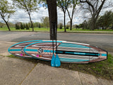 Two vibrant paddleboards & paddles lean on a tree, set for an RV rental adventure in the park.