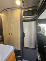 RV rental interior: Features a ceiling light, light wood cabinets, stainless steel microwave, and compact fridge.