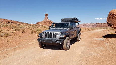 Silver Jeep Gladiator RV rental with rooftop tent on a desert off-road adventure, surrounded by red rock formations.