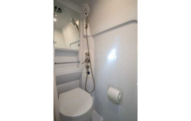 RV rental's compact bathroom, integrating a toilet and shower with convenient controls, a small mirror, and toilet paper holder.