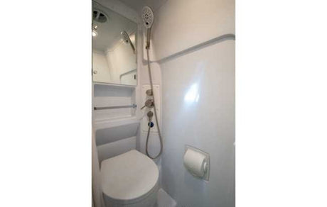 RV rental's compact bathroom, integrating a toilet and shower with convenient controls, a small mirror, and toilet paper holder.