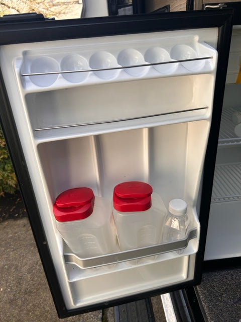 Practical RV rental fridge interior with door storage: eggs, a water bottle, and two containers with red lids.