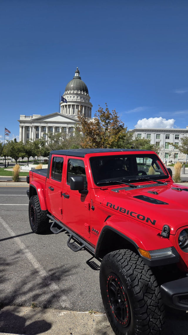 A striking red Jeep Gladiator Rubicon pickup is parked by a state capitol building. This adventure vehicle offers a different experience than an rv rental.