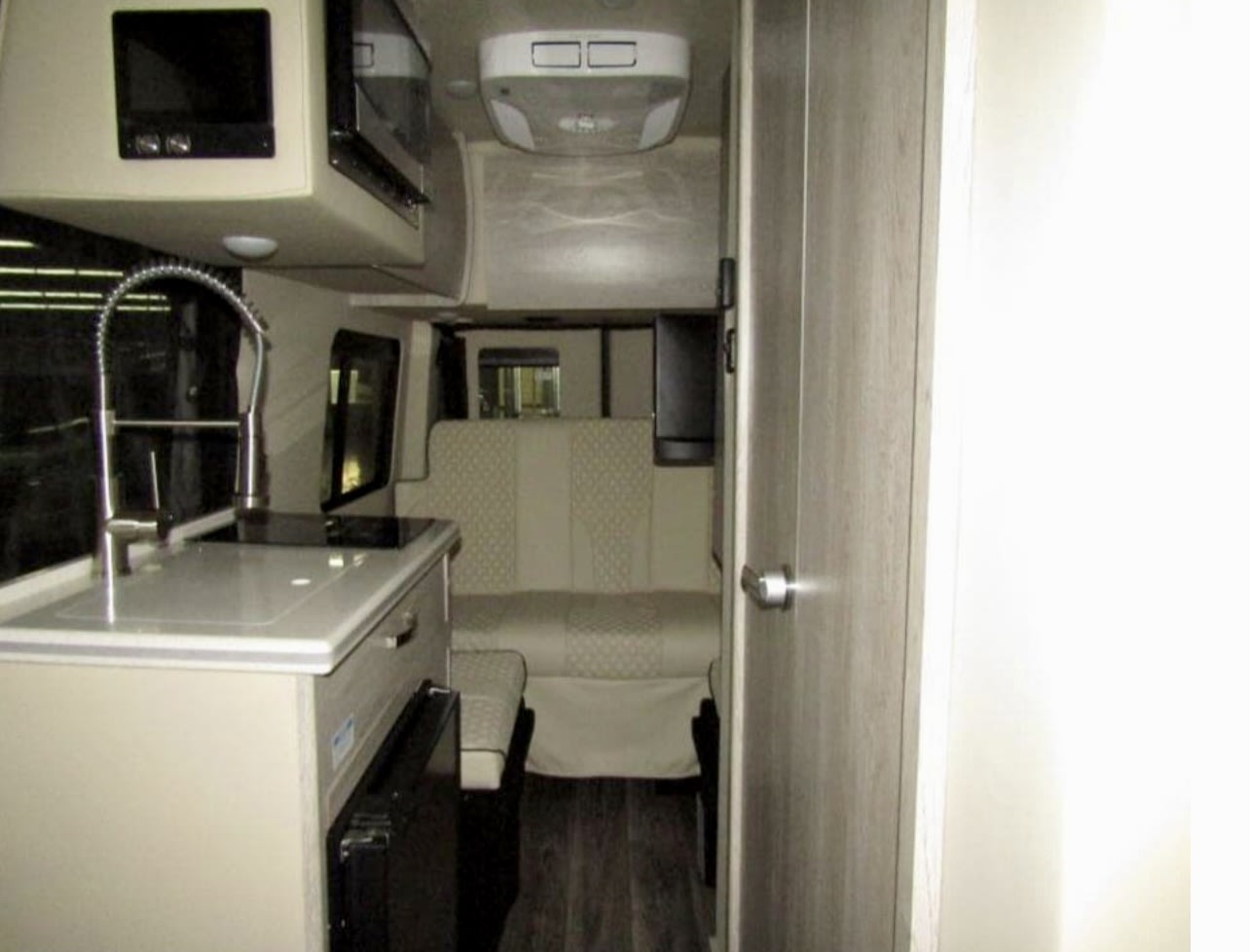 Modern rv rental interior, featuring a compact kitchenette with sink and microwave, plus a rear dinette for comfortable travel. — photo 6
