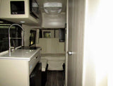 Modern rv rental interior, featuring a compact kitchenette with sink and microwave, plus a rear dinette for comfortable travel.