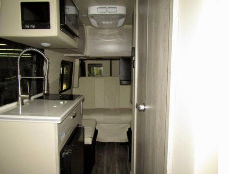 Modern rv rental interior, featuring a compact kitchenette with sink and microwave, plus a rear dinette for comfortable travel.