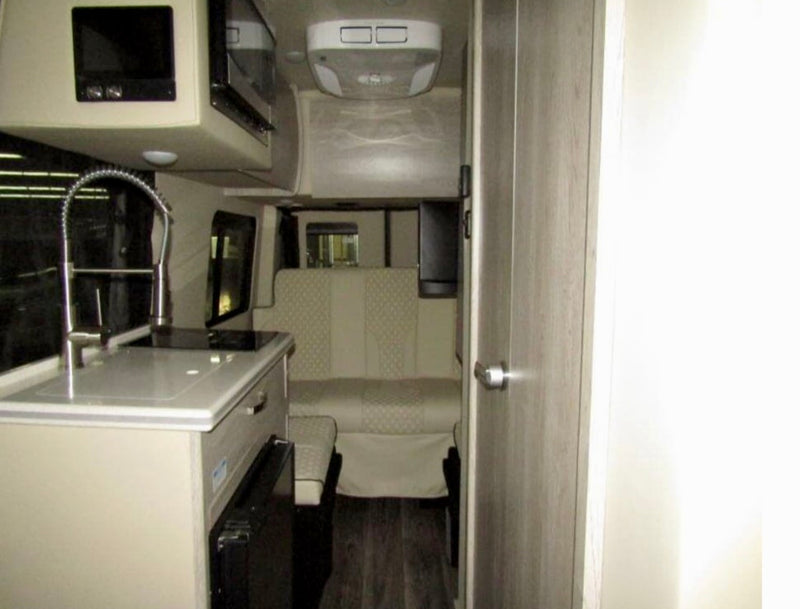 Modern rv rental interior, featuring a compact kitchenette with sink and microwave, plus a rear dinette for comfortable travel. — photo 6