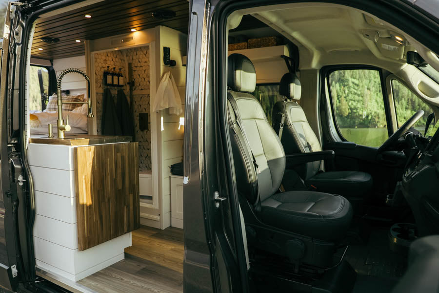 Inside a spacious rv rental camper van: modern kitchen, bath, and bed. Front seats overlook a scenic lake view, ready for adventure.