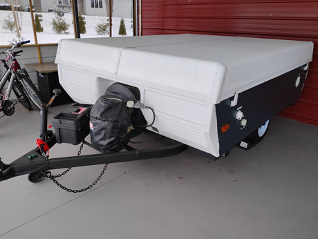 Compact white and dark grey pop-up camper with propane tanks and bikes. Ready for your next RV rental and camping travel adventure!