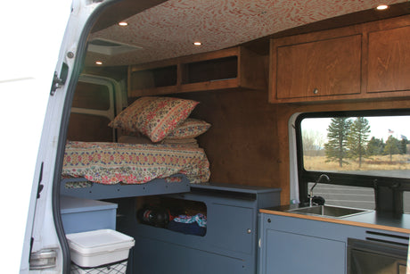 This rv rental shows a cozy, customized interior with a floral bed, blue storage, kitchen, and wood cabinets.