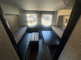 Spacious RV rental interior with dinette seating & tables, ready for your next adventure. Large windows show outside views.