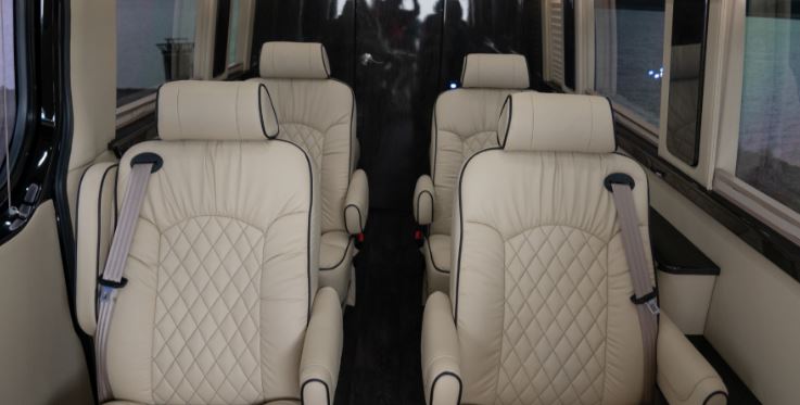  featuring cream captain's chairs with elegant diamond stitching.|Luxury RV rental interior showing two rows of cream leather captain's chairs with diamond stitching and seatbelts.|Inside a luxury RV rental: cream leather captain's chairs with a fold-out table and elegant wood trim for comfortable travel.|Inside an RV rental: Cream-colored