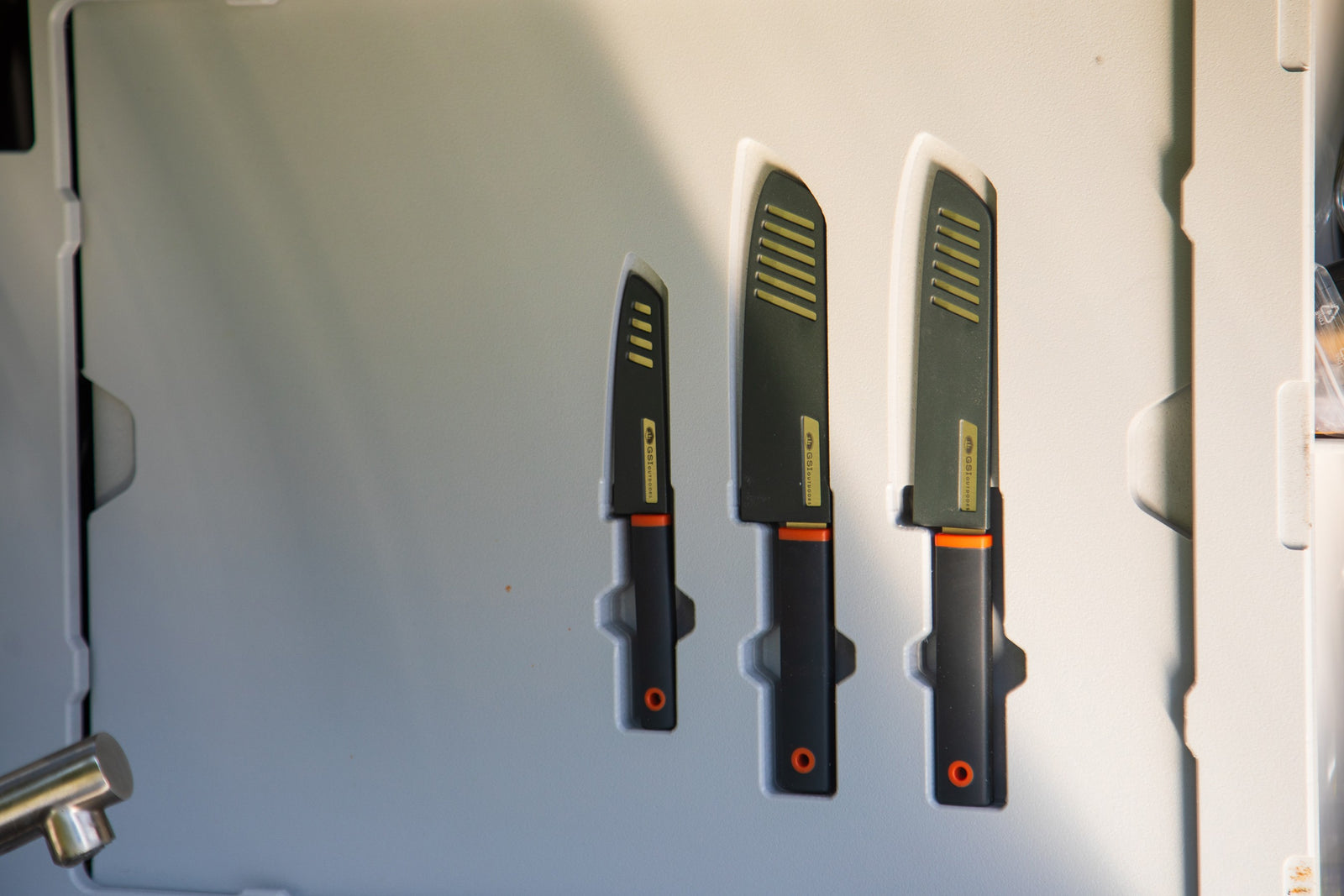 Organized GSI Outdoors knife set in an RV rental. Three black knives with orange handles and striped sheaths, perfect for cooking on the go.