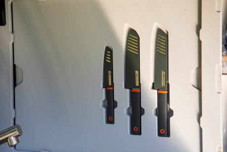 Organized GSI Outdoors knife set in an RV rental. Three black knives with orange handles and striped sheaths, perfect for cooking on the go.
