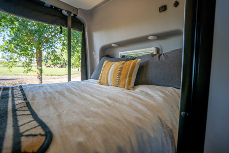 Cozy RV rental bedroom featuring a comfortable bed with a striped pillow and a serene view of nature outside the window.