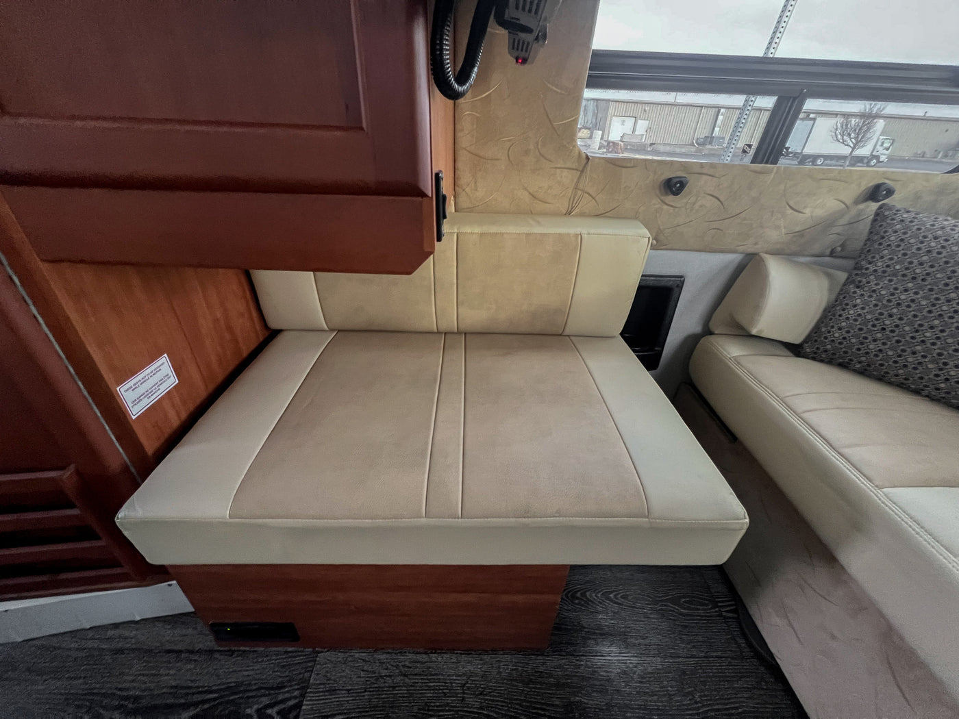 This RV rental interior features a cozy beige seat with a safety sign, perfect for relaxation while parked. — photo 15
