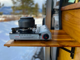 Winter RV rental cooking: Portable butane stove with a kettle on a wooden counter, outdoors in a snowy mountain setting.