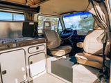 Explore this clean RV rental interior! Features a compact kitchen, comfy tan seats, and a bright cabin view.