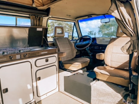 Explore this clean RV rental interior! Features a compact kitchen, comfy tan seats, and a bright cabin view.