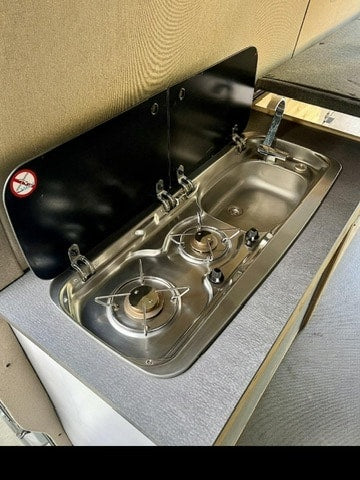 This RV rental's compact kitchen features a shiny stainless steel two-burner stove and sink with faucet, ideal for camper meals.