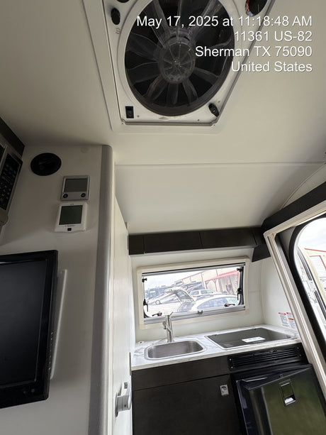 Explore this RV rental's compact interior, featuring a kitchen with sink and stove, refrigerator, overhead fan, and exterior view.
