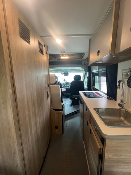 This RV rental interior features a compact kitchen, wood cabinetry, and a versatile front living area with seating.