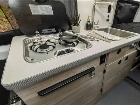 This RV rental's compact kitchen boasts a stainless steel stovetop, sink, and light wood cabinets for cooking on the road.