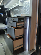 Modern RV rental interior with sleek kitchen drawers, a sink, hexagonal backsplash, and integrated LED lighting.