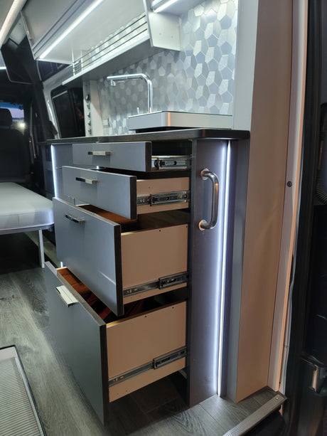 Modern RV rental interior with sleek kitchen drawers, a sink, hexagonal backsplash, and integrated LED lighting.