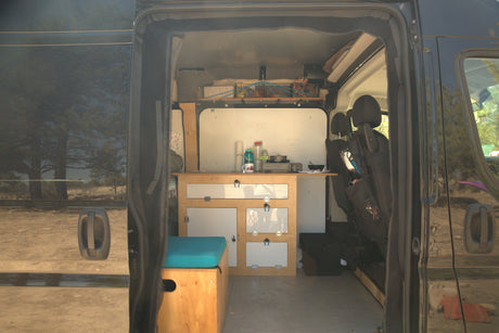 View into a custom camper van RV rental, showing a well-equipped kitchen, storage, and seating. Ideal for road trips!