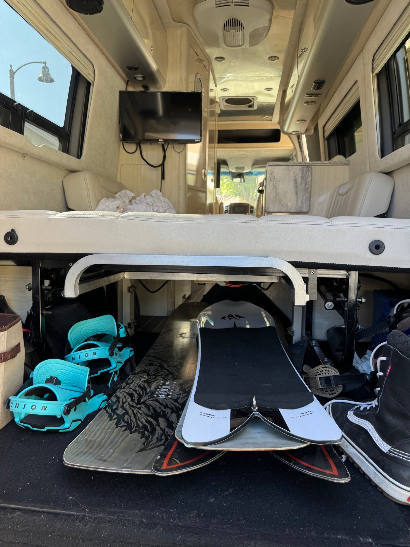 RV rental interior: snowboards, bindings, and boots neatly stored under a raised bed, with a mounted TV. — photo 15