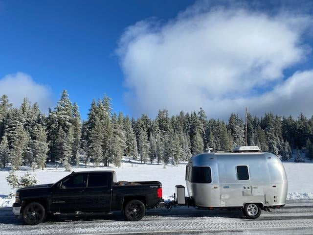 Winter RV rental adventure: A pickup truck tows an Airstream trailer through a beautiful snowy forest scene.