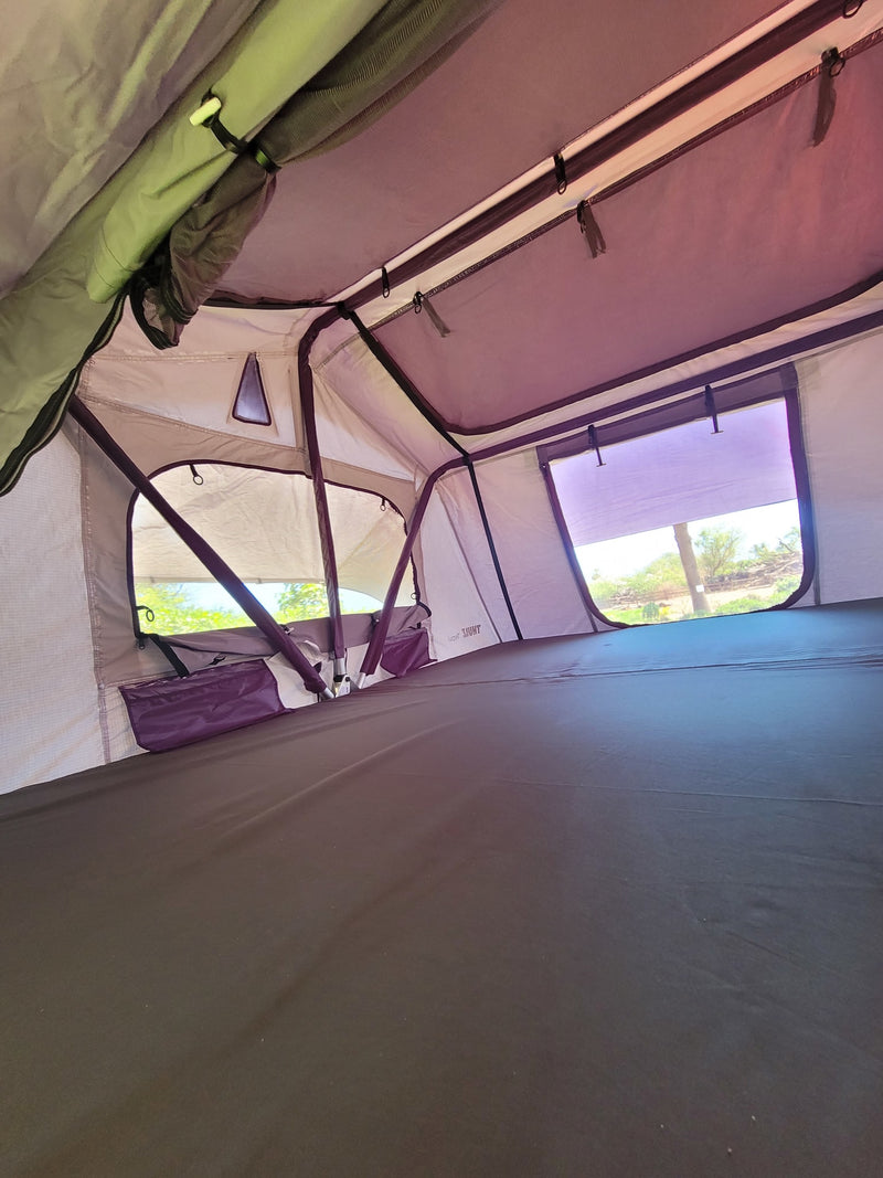 Inside a spacious roof-top tent, showing its dark mattress, windows with outdoor views, and storage pockets. — photo 15