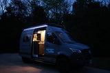 Grey Mercedes Sprinter RV rental parked at night, side door open with lit interior & bright exterior LED strip.