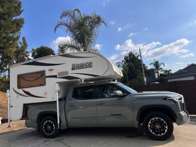  parked on a driveway. Ideal for an RV rental adventure.|A grey Toyota Tundra truck with a white Lance truck camper mounted. Ideal RV rental for outdoor trips.|A gray Toyota Tundra pickup truck with a white Lance truck camper mounted on its bed — photo 1